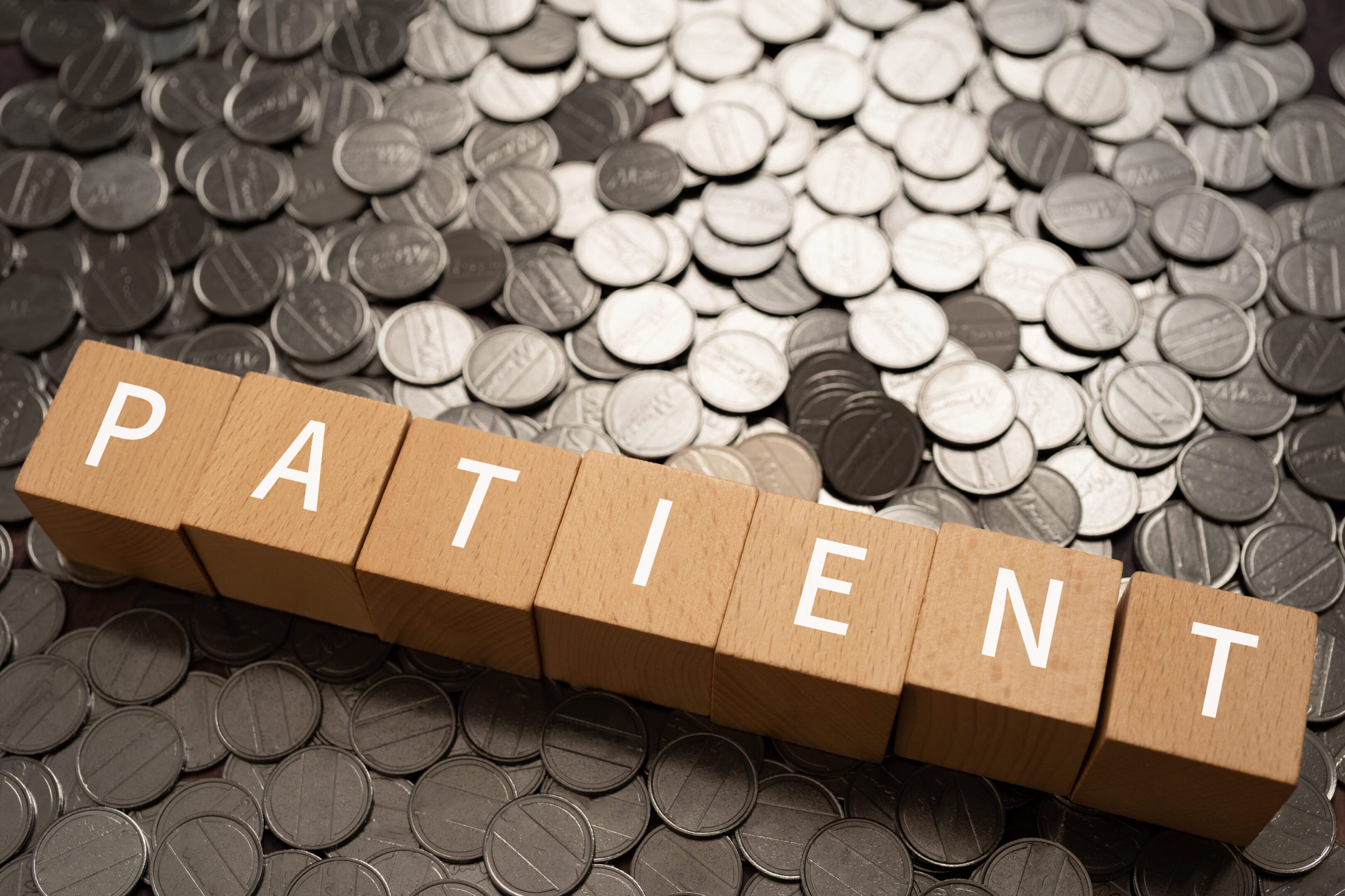 Wooden blocks with "PATIENT" text of concept and coins.