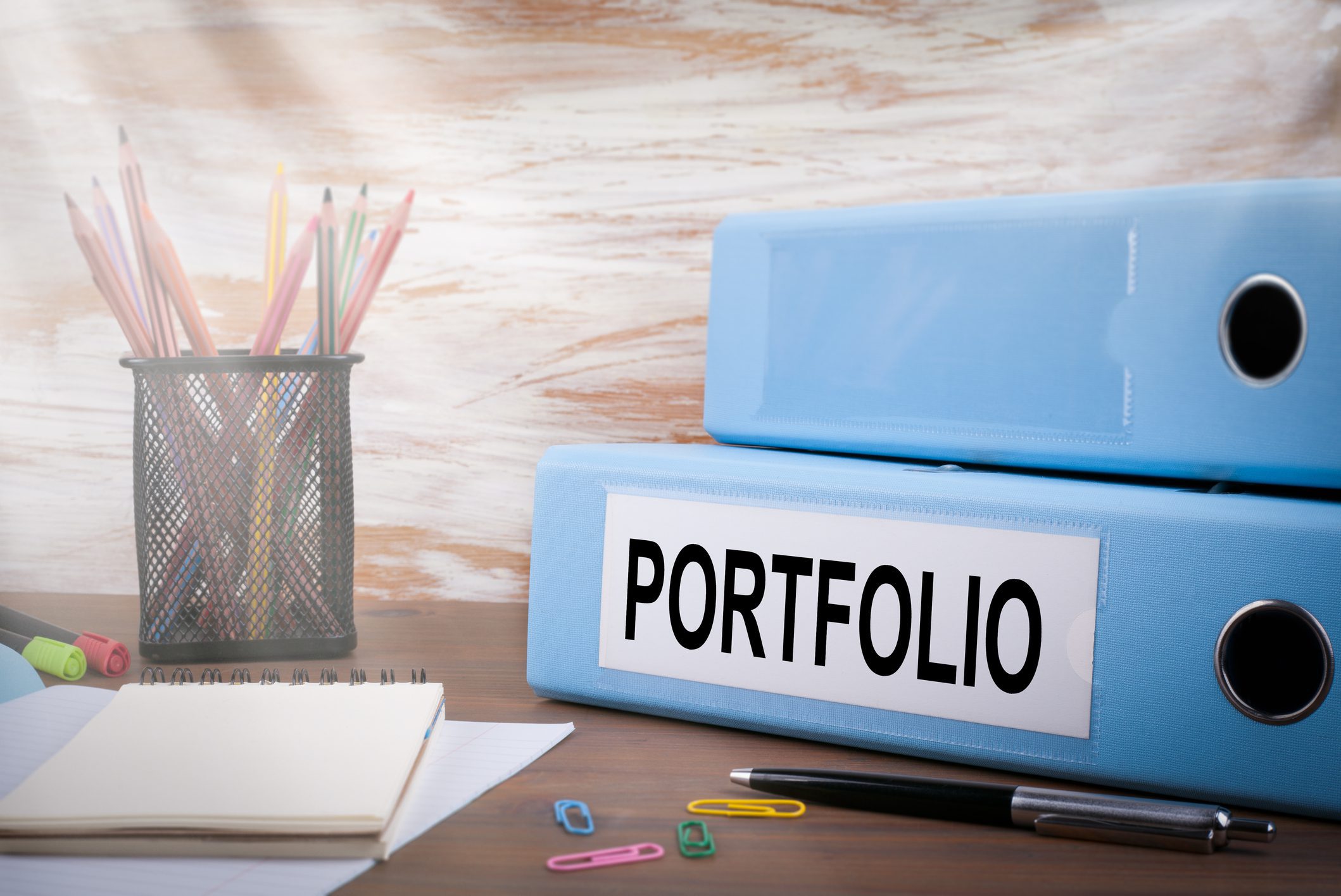 Portfolio, Office Binder on Wooden Desk. On the table colored pencils, pen, notebook paper.